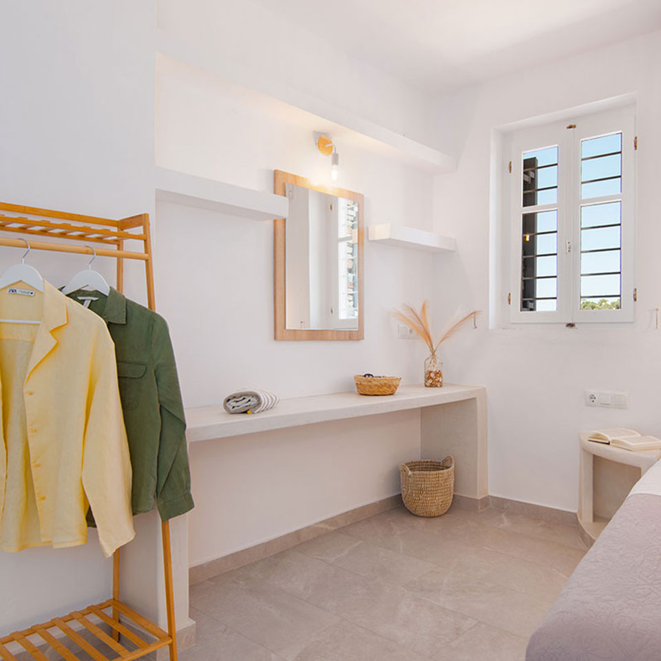 Μονό κρεβάτι σε υπνοδωμάτιο του Artemaki House στη Σίφνο με λευκούς τοίχους και ζεστό φωτισμό